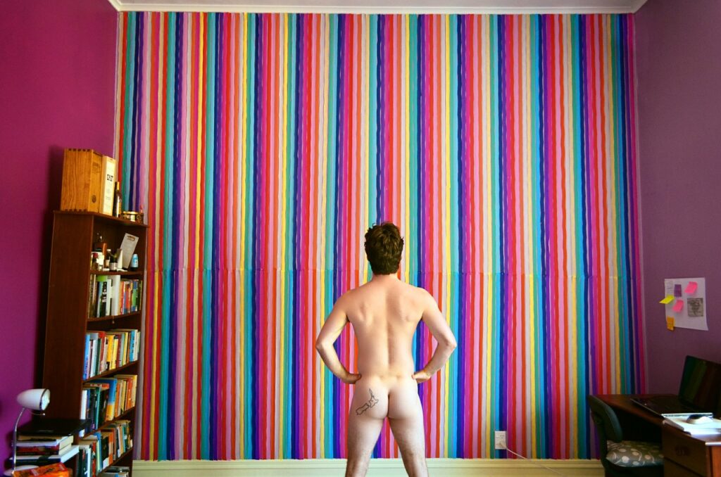 Butt Plugs VS Dildos; Are They Better Than Prostate Massagers? Nude man  staring at striped wall photographed from behind.