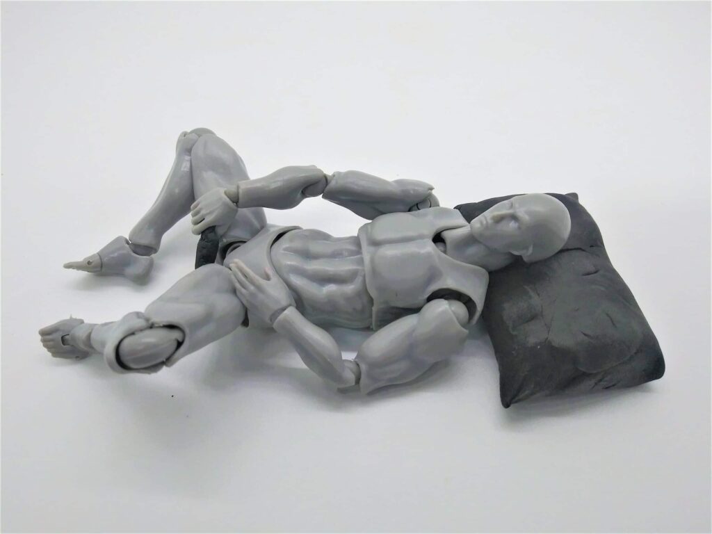 Positions for using a dildo for men: photo of a figure lying on his back, propped by a pillow and using a dildo for anal masturbation.