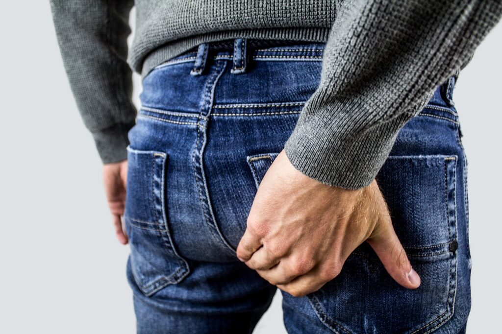 Wearing an anal plug to work, photo of a man's backside, clad in jeans, as he holds his bottom as if in pain.