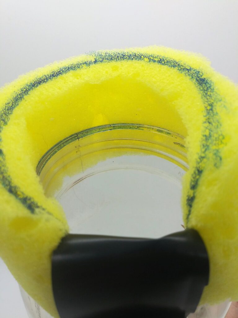 DIY penis pump; photo of step 10 showing the sponge being taped down around the mouth of the water bottle.