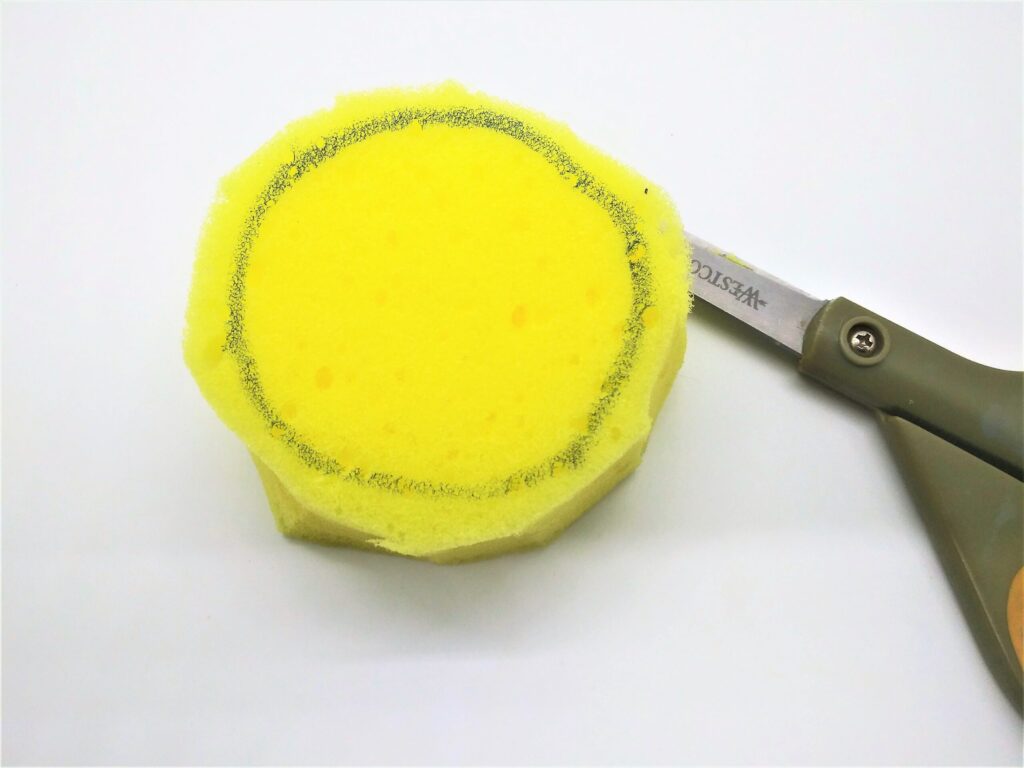 Homemade penis pump tutorial; photo of step 6 showing the circle being cut out of the sponge using scissors.