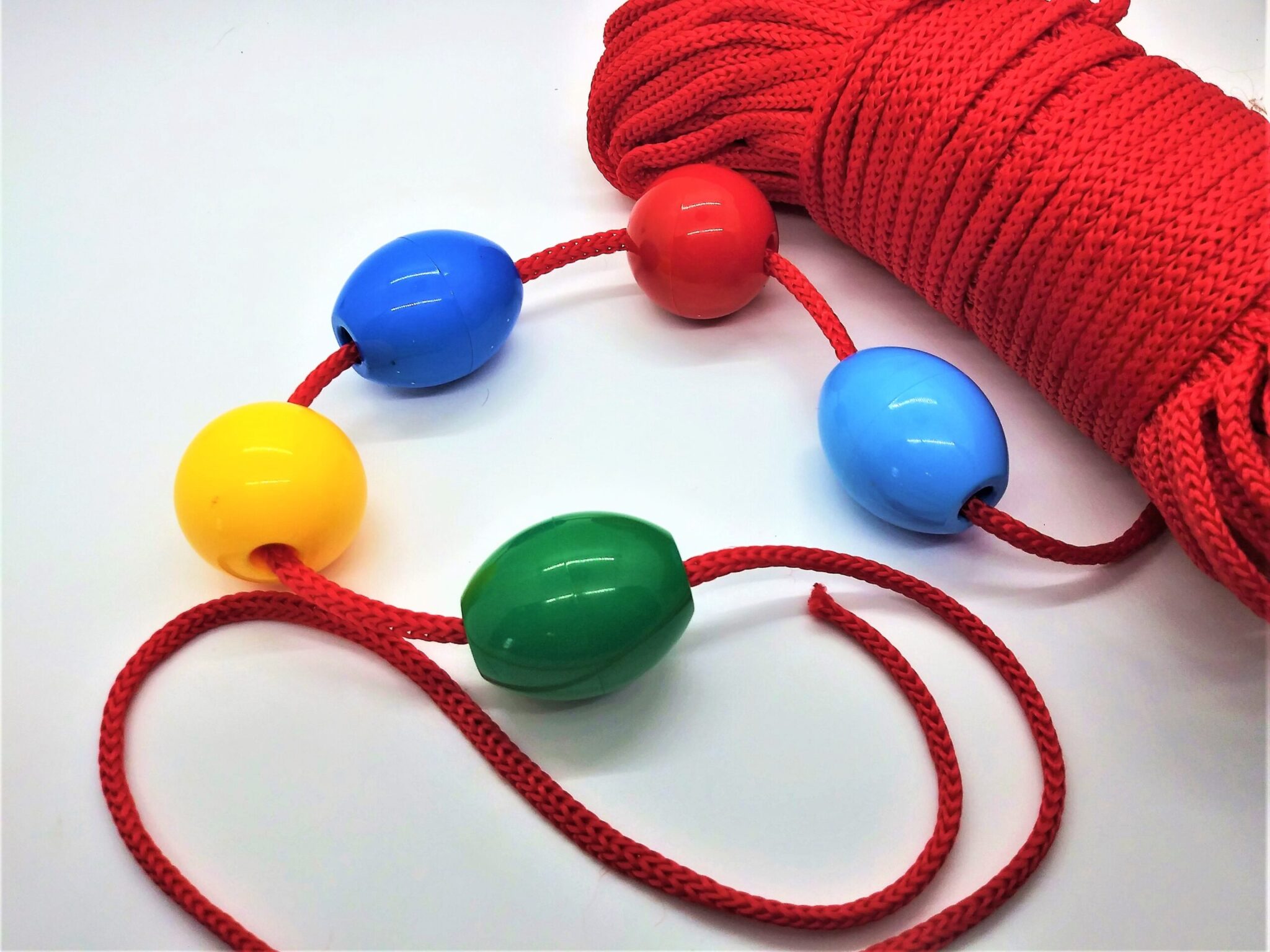 Homemade anal beads. Photo of 5 plastic beads strong on red rope to measure the proper length before cutting the rope.