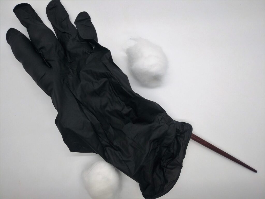 DIY anal sex toys made from a medical glove. Photo showing a chop stick being used to pack cotton balls into the finger of a black medical glove.
