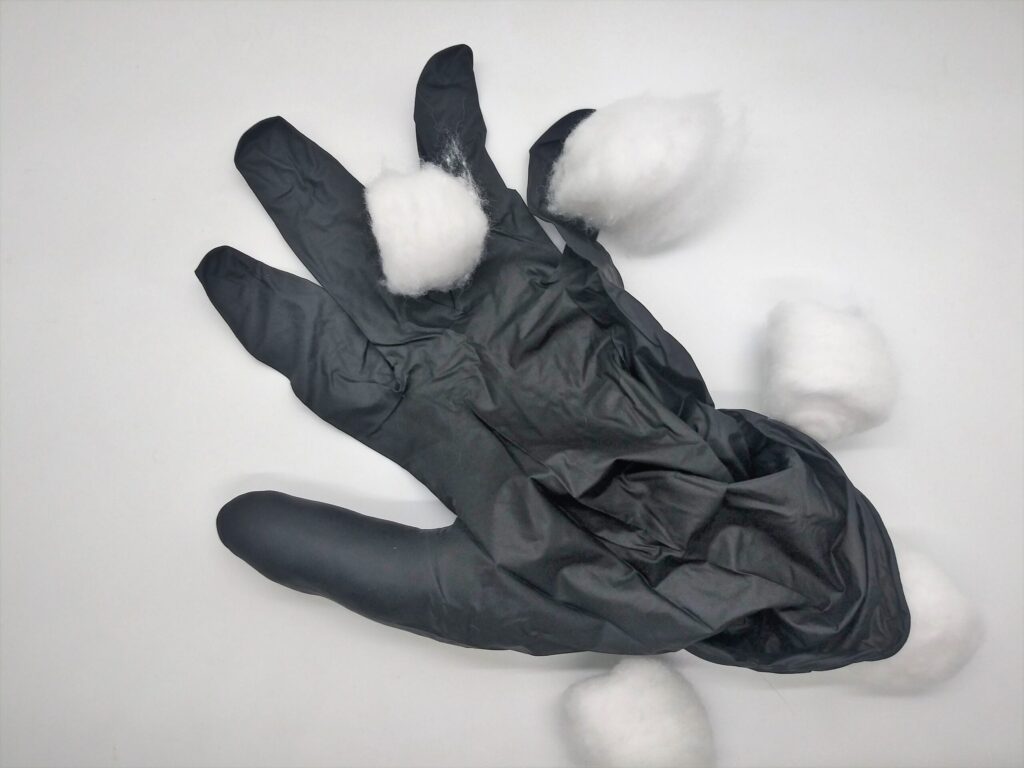 DIY anal sex toys with medical gloves, photo of cotton balls being placed into the fingers of a black medical glove.