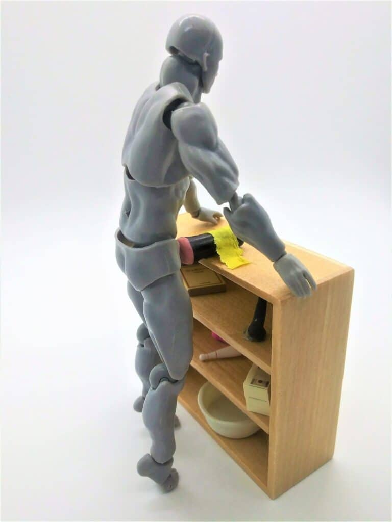 Photo of a male figure using a masturbator secured to the top of a small book case using duct tape.